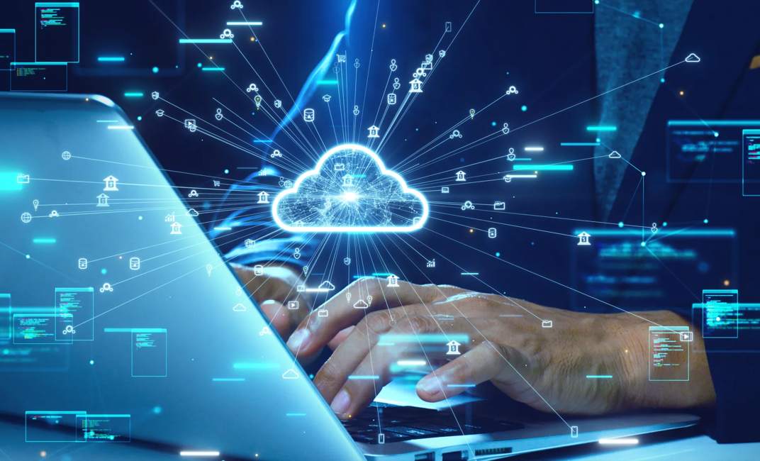 Close-up of hands typing on a laptop with a glowing cloud icon and digital data flow symbols representing cloud computing technology.